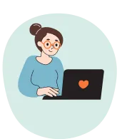 A woman wearing blue with glasses is sat at a laptop which has a red heart on it.